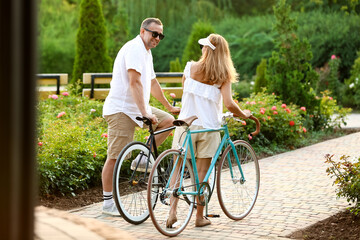 Mature couple with bicycles walking in city park on summer day