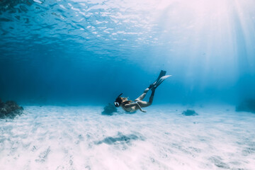 Woman freediver glides with fins over sandy bottom underwater ocean