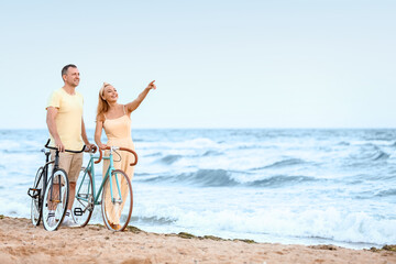 Fototapeta na wymiar Mature couple with bicycles walking along sea beach on summer day