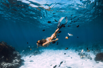 Beauty freediver lady with fins glides underwater with fishes in transparent ocean