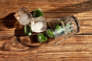 Transparent glass and Frozen fresh spinach in shape cubes on old wooden surface. Selective focus....