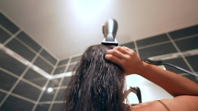 Woman drying hair with hair dryer in front of bathroom mirror