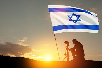 Silhouette of soldier kneeling with his head bowed with Israel flag against the sunrise in the...
