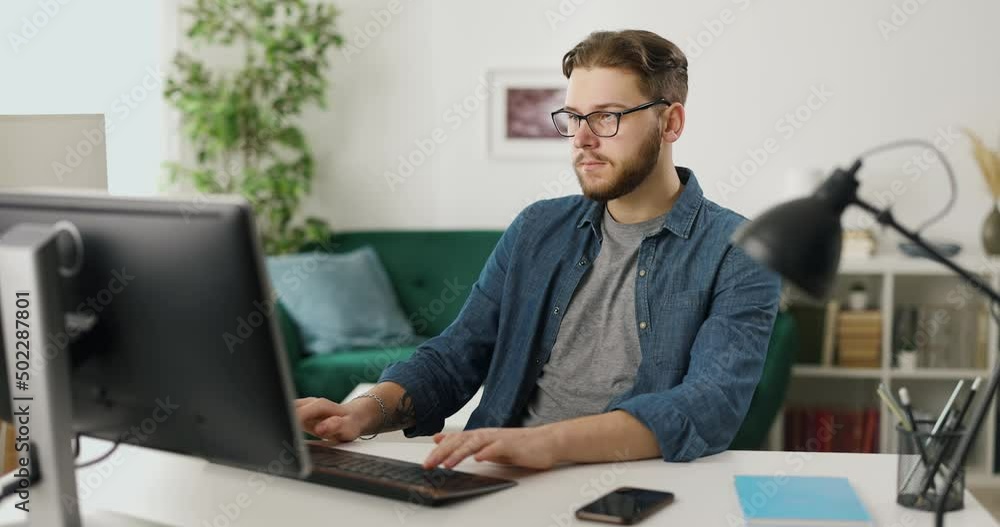 Poster professional programmer typing on pc keyboard while sitting at home office. young bearded man workin