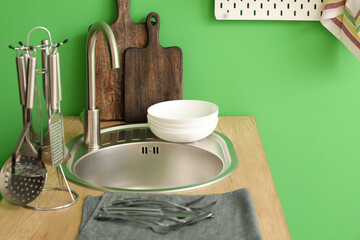 Wooden counter with silver sink and kitchen utensils near green wall