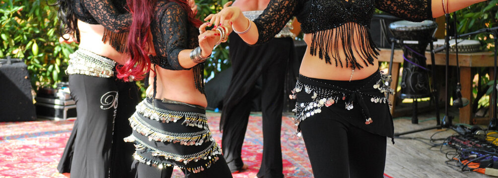 Bellydancers in colorful costumes on stage outdoors.