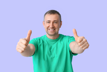 Mature man in green t-shirt showing thumbs-up on lilac background