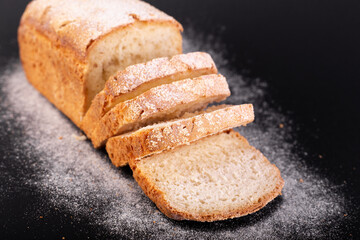 close up sliced french lean bread with flour on a black background. Concept recipe of handmade bread