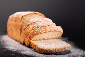 close up sliced french lean bread with flour on a black background. Concept recipe of handmade bread