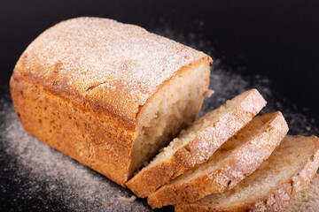 close up sliced french lean bread with flour on a black background. Concept recipe of handmade bread