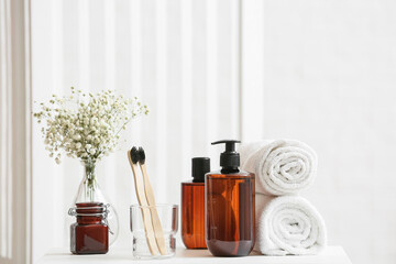 Holder with toothbrushes, bottles with cosmetic products and rolled towels on table