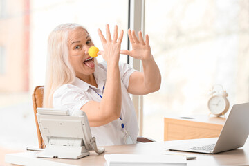 Funny mature woman with clown nose in office. April fools day celebration