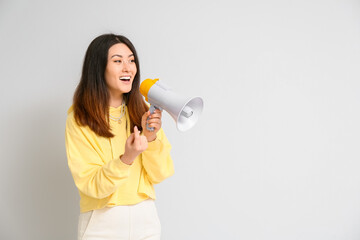 Young Asian woman with megaphone showing "come here" gesture on light background