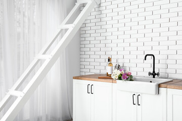 Sink with beautiful flowers and bottles of wine on counters near white brick wall