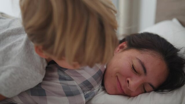 Little boy waking up mother in the morning jumping into mom and kissing