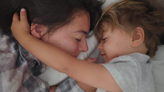 Mother child love and affection in morning bed waking up little boy loving mom family moment