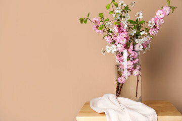Vase with blooming branches on table near beige wall