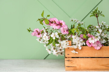 Wooden box with blooming branches on table near green wall