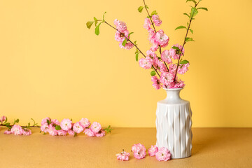 Vase with blooming branches on table near yellow wall
