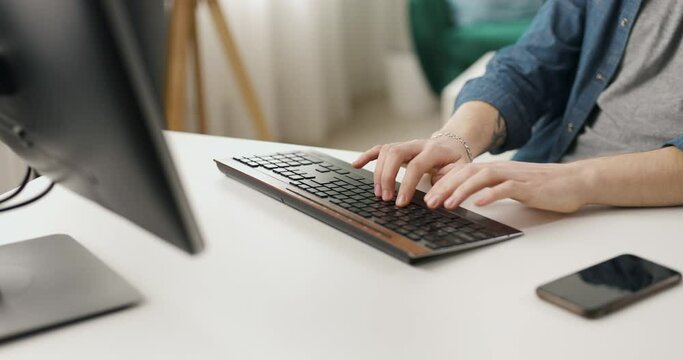 Close up of male hands typing on keyboard of modern pc. Caucasian man sitting at desk and using stationary computer for coding at home.