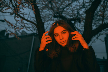 woman conceptual portrait in red light late evening in the park near flowering trees