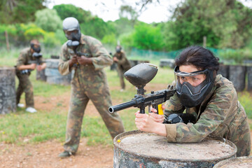 Excited male and female paintball players in protective uniform aiming and shooting with guns