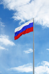 Russian white-blue-red flag is waving in front of blue sky and clouds