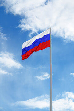 Russian white-blue-red flag is waving in front of blue sky and clouds