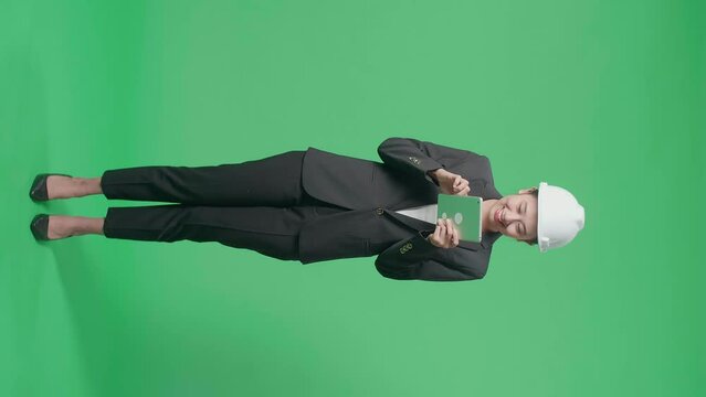 Full Body Of Smiling Asian Female Engineer Looking Around And Shaking Her Head While Using Tablet In The Green Screen Studio
