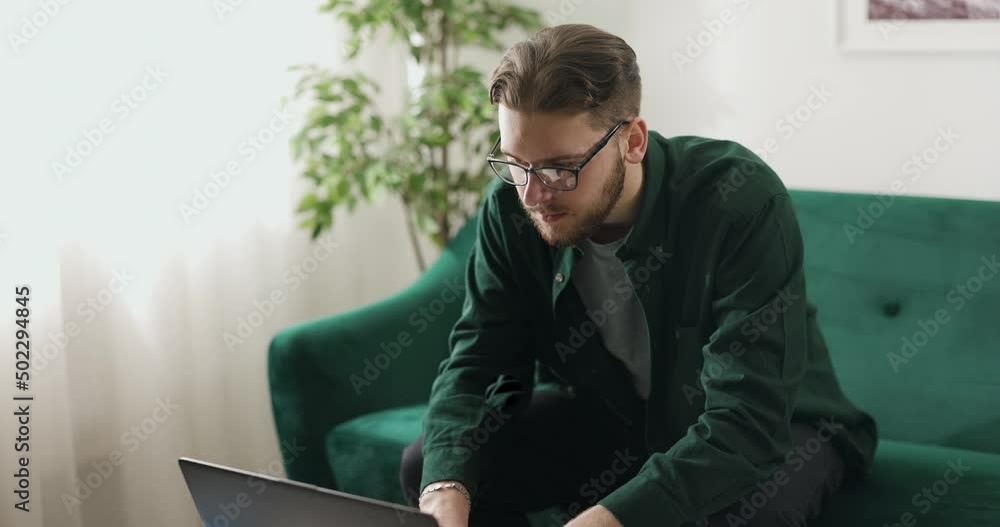 Poster focused bearded man in eyeglasses coding html and programming on modern laptop while working from ho