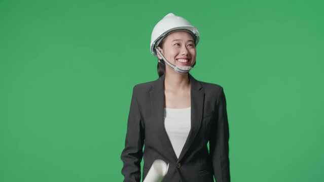 Smiling Asian Female Engineer With Blueprint Looking Around And Shaking Her Head While Walking In The Green Screen Studio
