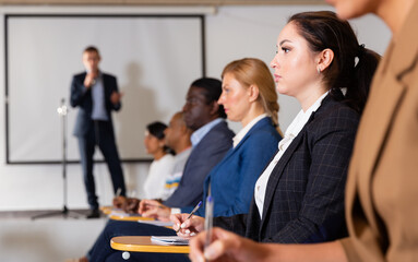 Portrait of female attentively listening to motivation lecture with colleagues at conference