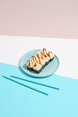 Baked Maki roll with shrimp and cheese on ceramic plate. Hot sushi roll with cheese topped on coloured background. Japanese menu concept. Hot sushi roll in modern style.