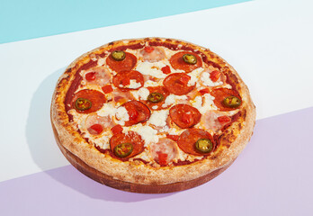 Italian pizza with ham, pepperoni and jalapeno on coloured background. Meat pizza with salami and chilli pepper in minimal style on blue color. American pizza delivery concept with color backdrop