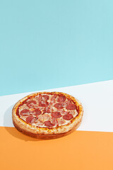 Italian pizza with salami, ham, bacon, pepperoni on coloured background. Meat pizza with sausage and bacon in minimal style on blue, orange color. American pizza delivery concept with color backdrop.