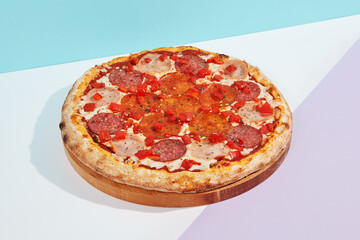 Italian pizza with salami, ham, pepperoni and paprika on coloured background. Meat pizza with salami and pepperoni in minimal style on blue color. American pizza delivery concept with color backdrop.