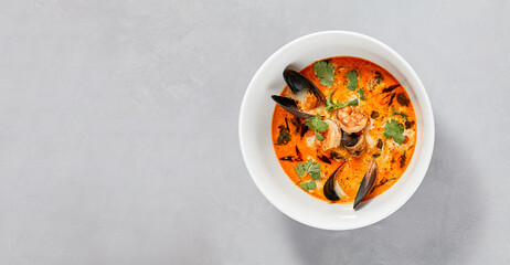 Traditional asian food - tom yam kung with prawn and mussels. Tom yum soup with seafood and coconut milk. Tom yam in ceramic bowl on gray stone background. Oriental cuisine. Asian menu. - obrazy, fototapety, plakaty