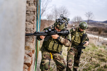 Two men soldiers in uniform braking in to the house ruin during mission battle operation dogs of war volunteers mercenaries contractor secure the building armed service holding rifles pointed