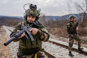 Two soldiers dogs of war mercenaries men in uniform armed service rifles aiming gun while securing the railroad in combat zone in war military battle observing territory patrolling area during mission - obrazy, fototapety, plakaty