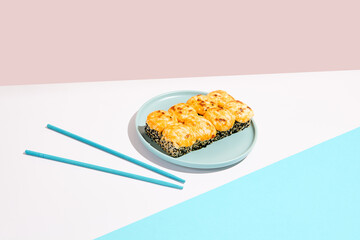 Hot maki roll with cheese and sesame on coloured background. Baked sushi roll with salmon inside, sesame outside, cheese topped. Maki sushi in minimal style. Japanese menu concept.