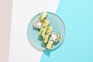 Fresh maki roll with crab on coloured background. Sushi roll with crab and cheese inside, cucumber and lemon outside. Green Maki sushi in minimal style. Japanese menu concept.