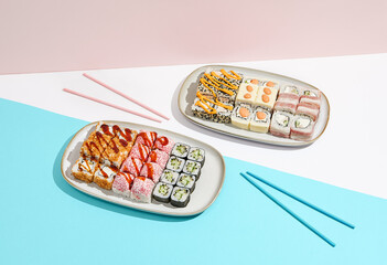 Sushi set on ceramic dishware with coloured chopsticks. Trendy set of maki sushi in minimal style. Modern japanese menu concept. Maki sushi assorted on coloured background.