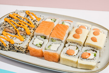 Sushi set on ceramic dishware with coloured chopsticks. Trendy set of maki sushi in minimal style. Modern japanese menu concept. Maki sushi assorted on coloured background.