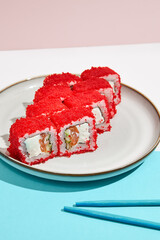 California maki roll with tobiko caviar on modern coloured background. Sushi roll with salmon and cucumber inside, tobiko caviar outside. Colourful maki sushi in minimal style. Japanese menu concept.