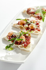 Beef tartare on crispy focaccia isolated on white background. Appetizer from minced meat with spicy sauce on toast.  Starter food meat tartare in French style. Contemporary food for restaurant.