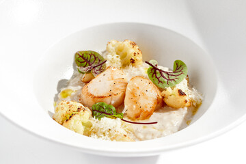 Delicious creamy risotto with sea scallop and cauliflower. Elegant main course with seafood on white plate. Grilled scallop with cauliflower and creamy rice. Seafood risotto with scallops.
