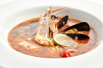 Tomato seafood soup in plate isolated on white background. Seafood stew Cioppino - shrimp,  mussels and salmon in tomato broth. Seafood dish in Italian restaurant menu.