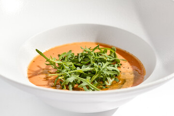 Summer Spanish soup - gazpacho with rocket salad isolated on white background. Vegetarian cold tomato soup in white plate. Meatless food in menu. Veggie lunch. Healthy food. Plant based eating.