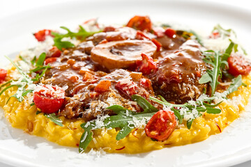Traditional Italian dish - osso buco with risotto Milanese and cherry tomato and rucola. Ossobuco with saffron rice isolated on white background. Stewed meat on bone with yellow risotto.