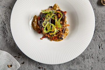 Braised beef cheeks with pearl barley and celery in creamy mushroom sauce. Veal cheek with mushroom risotto on gray stone background. Main course concept. Food menu for restaurant.